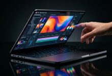 MacBook Pro warna Space Black dengan layar sentuh OLED yang sedang disentuh jari di studio gelap